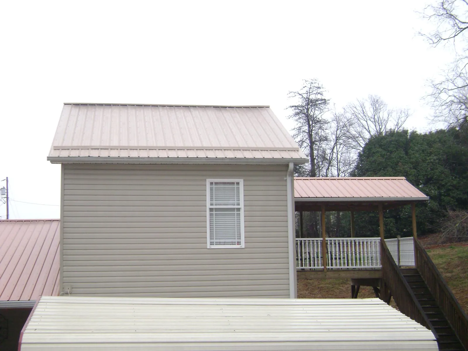 Tan metal roofs on a two story addition and attached porch, from a Roof Replacement job in Beverly